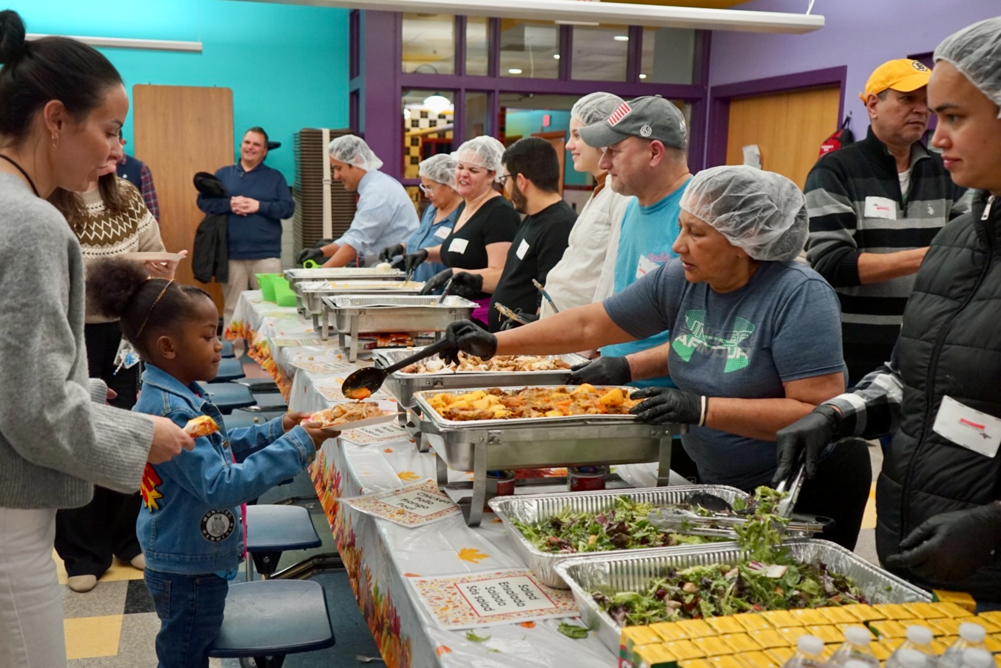 A young girl being served food at a Thanksgiving gathering in a school cafeteria